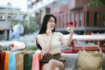A stylish Asian woman walks happily outside a luxury shopping mall, holding bags from recent...