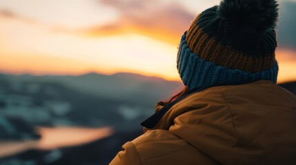 Person in a beanie looking at sunset over mountains.