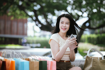 A cheerful young Asian woman, stylishly dressed, smiles excitedly while holding shopping bags....
