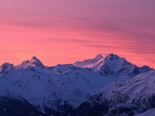 Early morning light casts a warm glow on snow-covered peaks under a bright pink sky, highlighting the beauty of the mountainous landscape