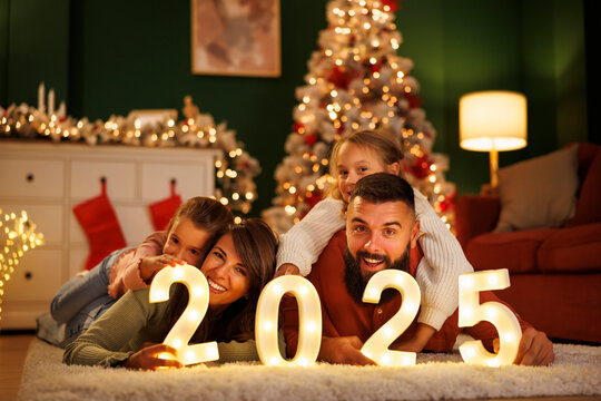 Parents and children holding numbers 2025 while spending New Year's Eve at home