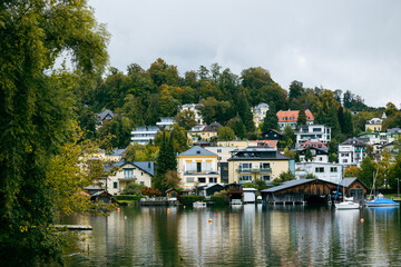 Fototapeta premium Colorful houses and buildings on the hillside by a lake, with reflections in the calm water. The scene captures a quaint lakeside village with a peaceful and picturesque atmosphere