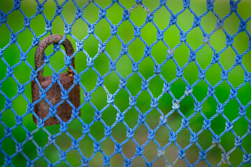 Rusty Padlock Hanging on a Blue Netting Background