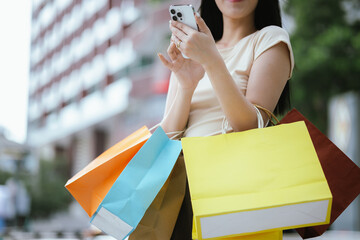 A cheerful young Asian woman holds shopping bags with a bright smile, excited by her summer...