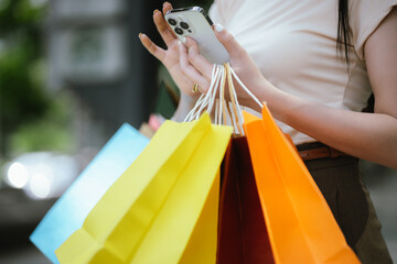 A cheerful young Asian woman holds shopping bags with a bright smile, excited by her summer...