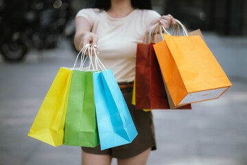 A cheerful young Asian woman holds shopping bags with a bright smile, excited by her summer shopping experience. Stylish and energetic, she enjoys the privilege of retail therapy while traveling in a 
