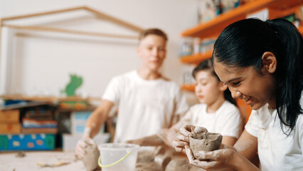 Caucasian boy modeling bowl of clay while cute asian girl working on dough at pottery workshop. Skilled highschool student playing on dough while wear muddy shirt at art lesson. Creative. Edification.