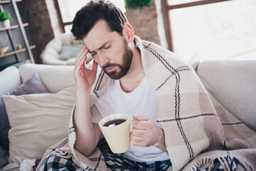 Photo of young ill man wearing sleepwear staying home feeling bad drinking tea sitting on sofa...