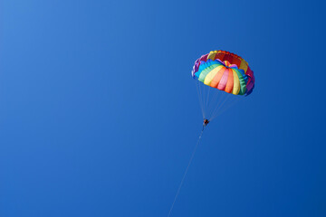Tourists fly on a bright paraglider against the blue sky in the summer on a sunny day. Beach holidays, tourist marine entertainment. Parasailing