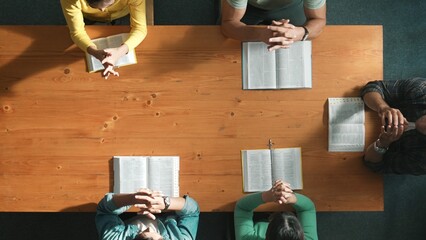 Top down aerial view of smart team hold hands on the holy bible and praying god while sitting at...