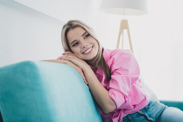 Naklejka premium Young woman in pink shirt enjoys relaxing on sofa at home in bright daylight