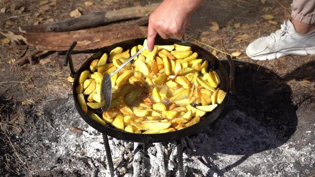 Cooking food on a campfire while hiking. Fried potatoes. Frying on a fire outdoors. Camping food in nature. Stir the vegetables in the pan