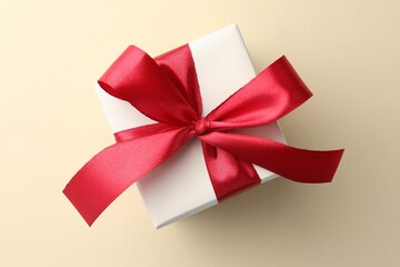 Beautiful gift box with red bow on beige background, top view