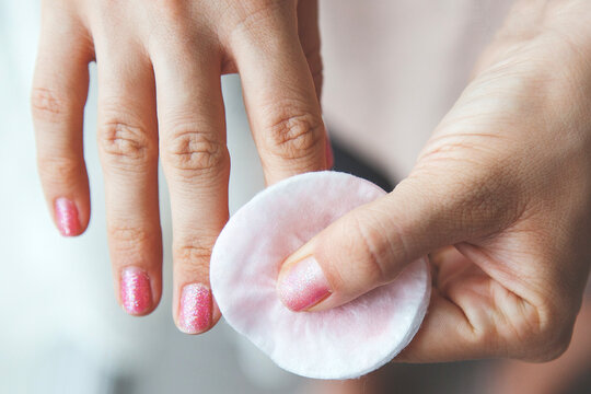 close up of female hand with shiny pink nail polish removing polish with cotton pad and nail polish remover