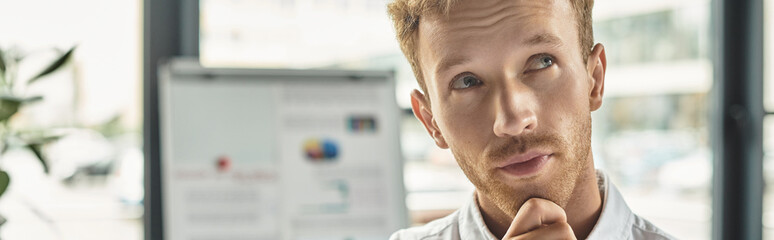 A redheaded businessman in a white shirt contemplates ideas while working in a contemporary office setting.