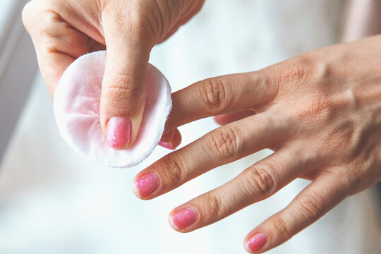 close up of female hand with shiny pink nail polish removing polish with cotton pad and nail polish remover