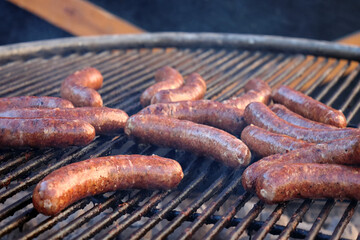 Close-up of large beef sausages being grilled on an open grill with a grate.