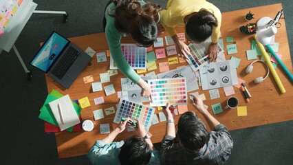 Top down aerial view of skilled designer hold logo while discuss with team. Aerial business group...