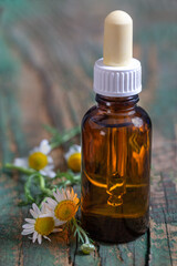 Small glass bottle with essential roman chamomile oil on the old wooden background. Chamomile flowers, close up. Aromatherapy, spa and herbal medicine ingredients. .