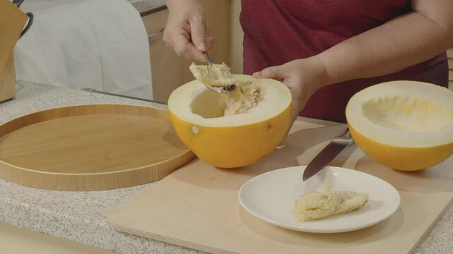 Woman's hand removing seeds from a cut melon with a spoon
