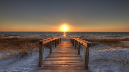 Fototapeta premium A tranquil wooden walkway approaches the beach as the sun sets, casting warm hues over the ocean and highlighting the grassy dunes