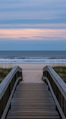 Fototapeta premium A tranquil wooden walkway approaches the beach as the sun sets, casting warm hues over the ocean and highlighting the grassy dunes