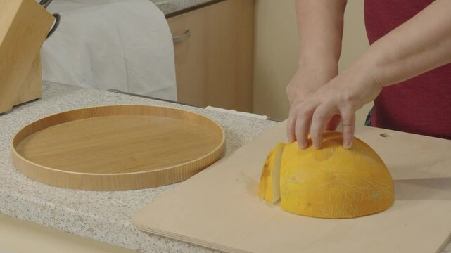 Woman cutting half a melon into slices with a knife