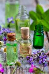 Selection of essential oils, with herbs and flowers in the background