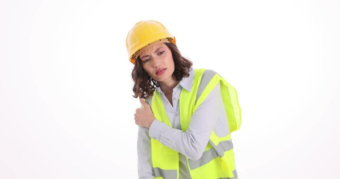 Architect woman in safety vest and helmet touches hurt shoulder on white background. Injured construction worker massages arm to relive pain