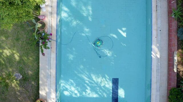 Wired automatic submersible vacuum cleaning robot that sweeps the floor and walls of the pool in the water. Aerial drone shooting