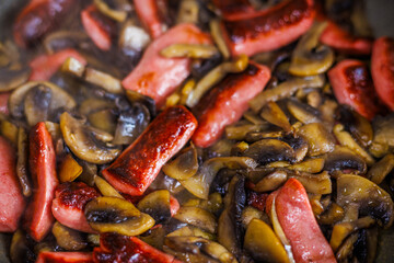 closeup view of roasting cut champignon mushrooms and sausages.