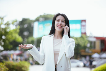 Fototapeta premium Active Asian woman in suit standing outdoors in city holding smartphone and laptop. She represents the future of finance and investment, keeping updated on news and opportunities.