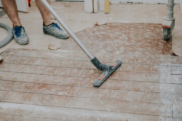 A young man vacuums the floor with a construction vacuum cleaner.