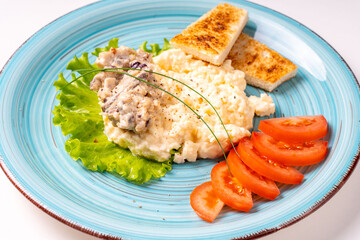 Scrambled eggs with mushrooms and crispy toast, garnished with lettuce and tomatoes, on a turquoise plate, on a white table with a burgundy napkin and cutlery. Delicious and healthy breakfast.