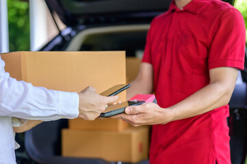 Close-up of a male delivery man holding a parcel box as he delivers the parcel to a female customer at home, paying cash on delivery with a QR code.