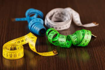 Tailor's measuring tapes of different colors lie on a dark wooden table. Selective voicing. Place...