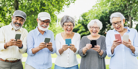 Group of senior adult friends laughing while using smartphones in the park