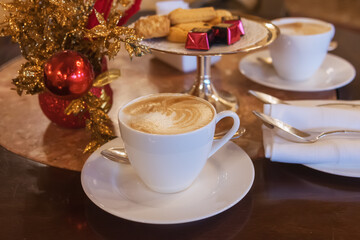 A cup of cappuccino on a table with Christmas decor