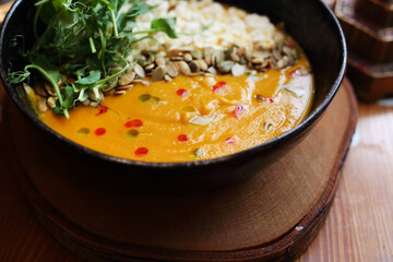 Creamy pumpkin soup, with smoked cottage cheese, seeds, fresh greens, close up. Vegetarian soup in Jewish restaurant.