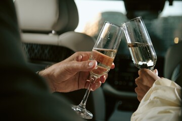 Over shoulder shot of celebrity couple enjoying sparkling champagne celebrating success sitting in back seat of car on river bank, fish eye effect