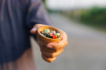 Hand Holding Wooden Bowl of Assorted Pills and Capsules Healthcare and Medication Concept