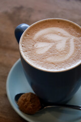 Picture of a cup of coffee on a wood table. Chai latte in a mug. White latte art with a heart. Morning breakfast, working at the cafe.