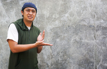 Confident Asian Man Presenting Product or Idea Against Concrete Wall