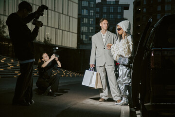 Fashionable man in grey classy suit helping girlfriend get out of car just arrived from shopping,...