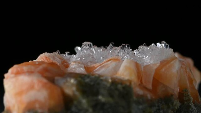 Clear Natrolite crystals on Orange Gmelinite (from Glenarm, N. Ireland) sample rotating against a black background.