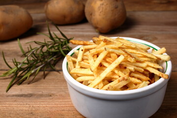 Fried potato sticks in a bowl and arranged on a wooden table.