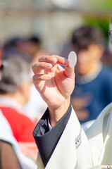 hand of a catholic priest elevating the host in the sacrament of communion at an outdoor service, religion concept