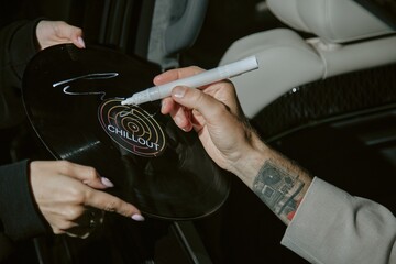 Close up on hand of famous musician signing vinyl music record with white marker sitting in car at...