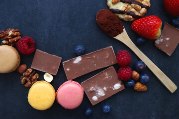 Macarons, chocolate, cookies, berries and various nuts on dark blue background. Top view.