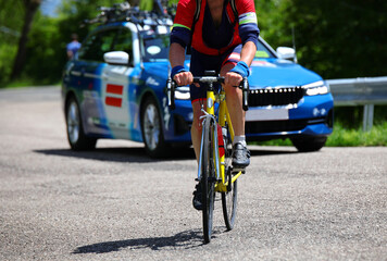 cyclist with racing bike pedaling uphill during training and the sports team car following him to...